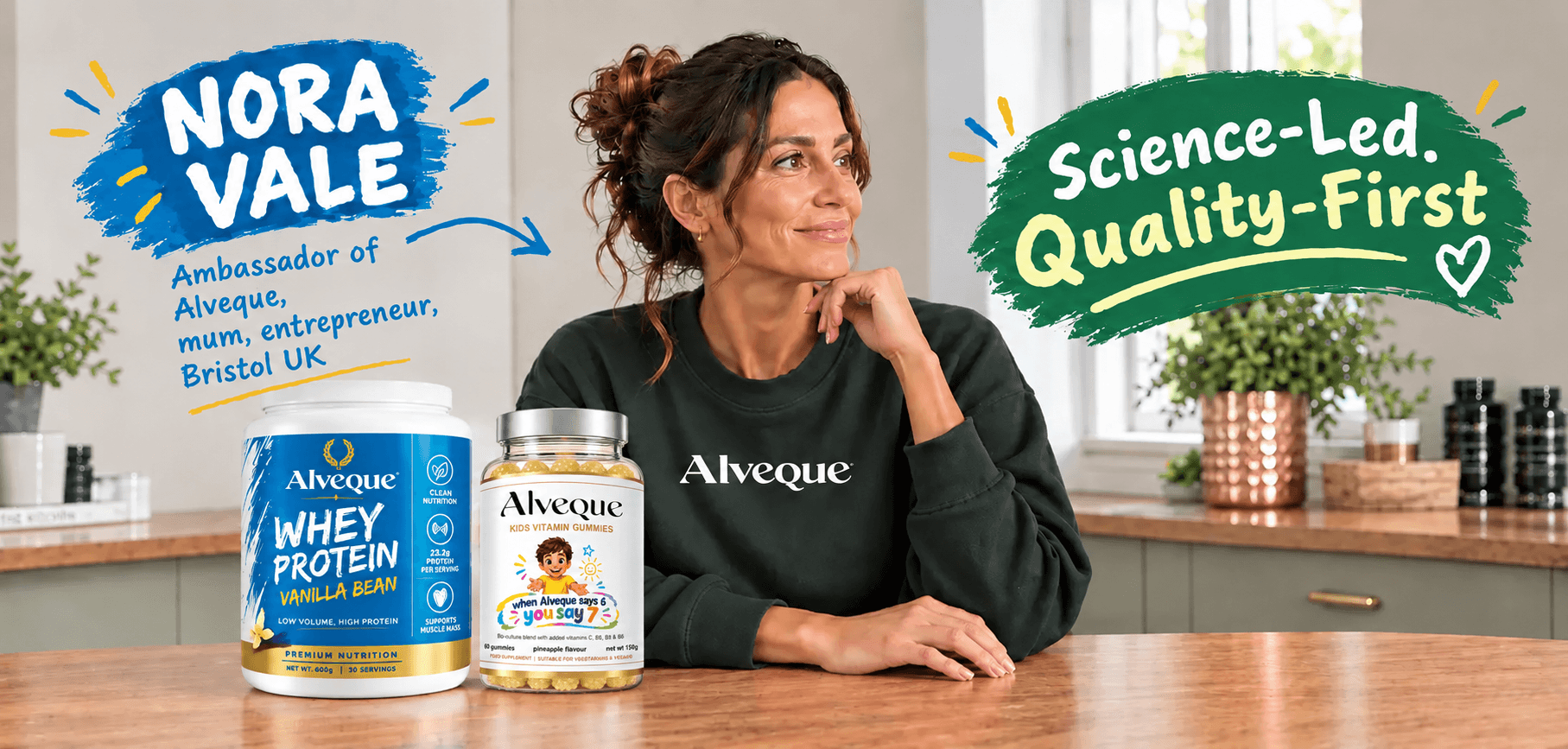 Nora Vale, founder of Alveque, sitting at a wooden table with a laptop and an Alveque shaker bottle